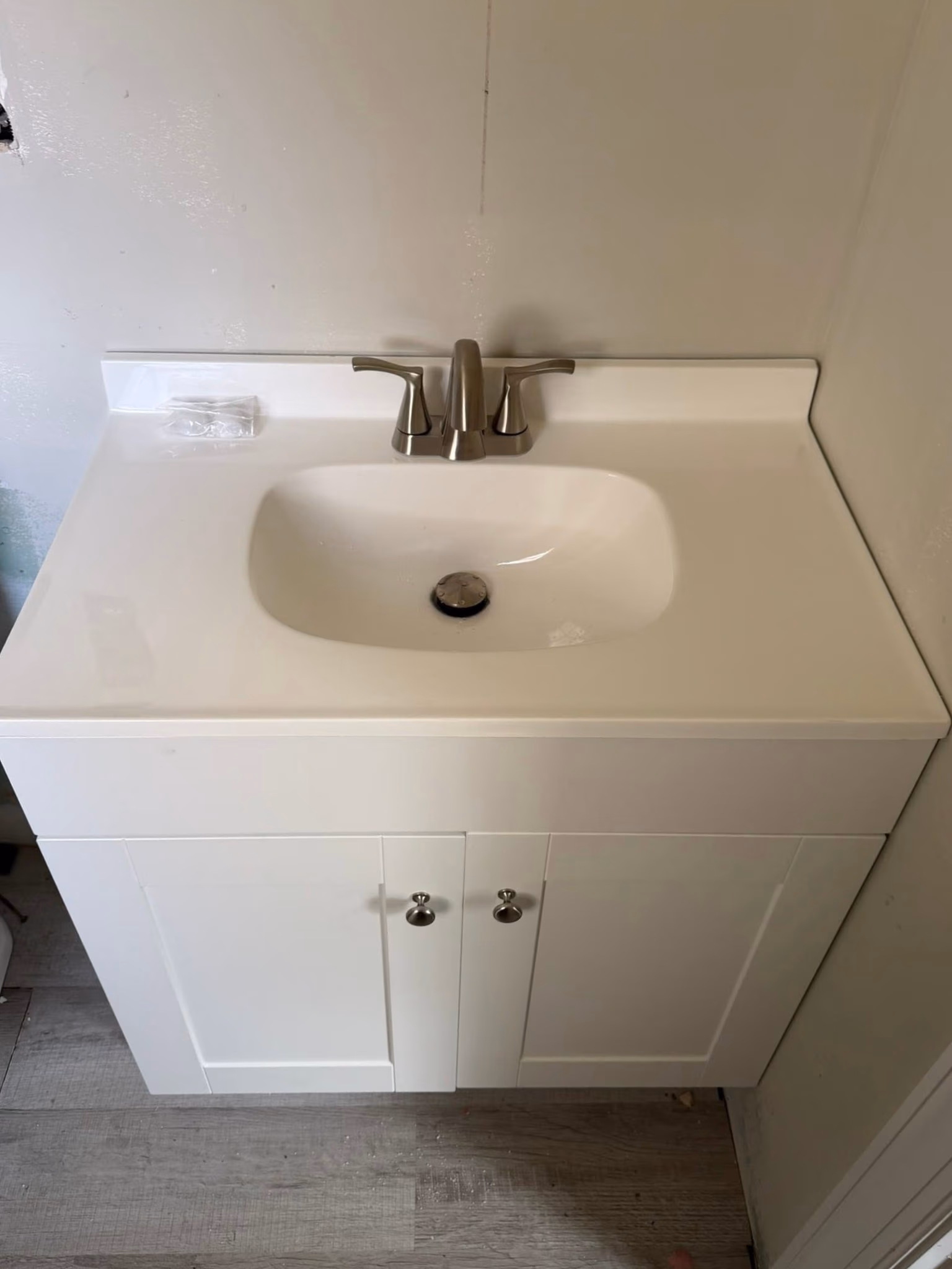 White bathroom sink with stainless steel faucet and storage cabinet below on wood floor.