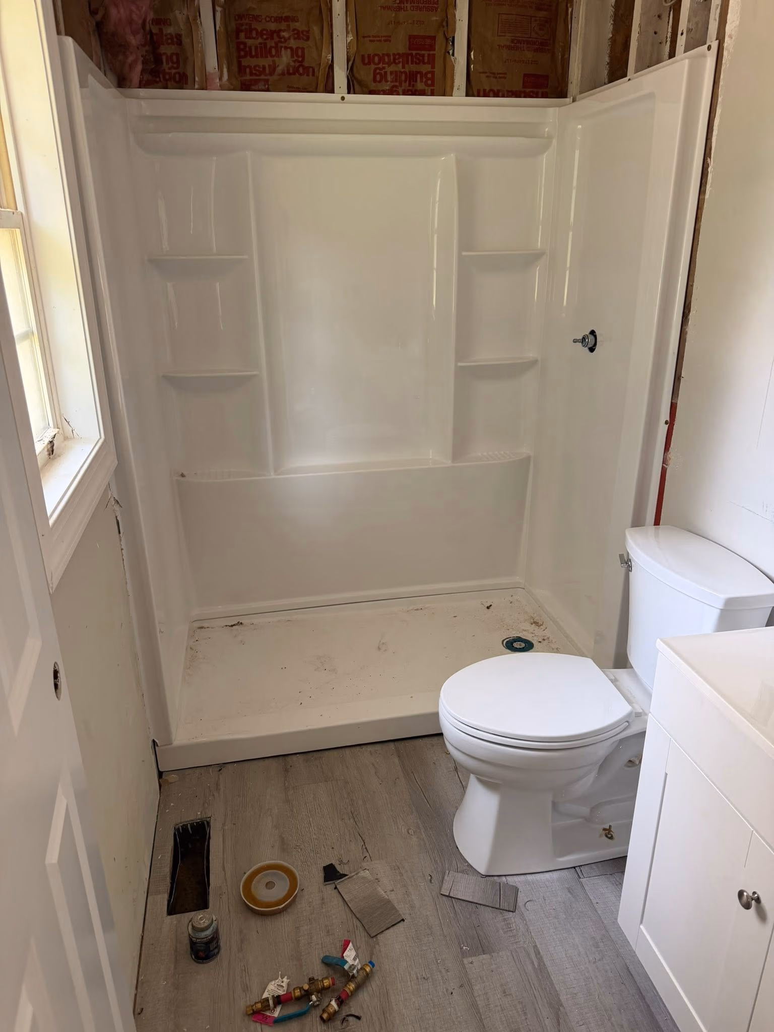 Partially remodeled bathroom with new white toilet, white shower stall, and scattered construction debris on the floor.