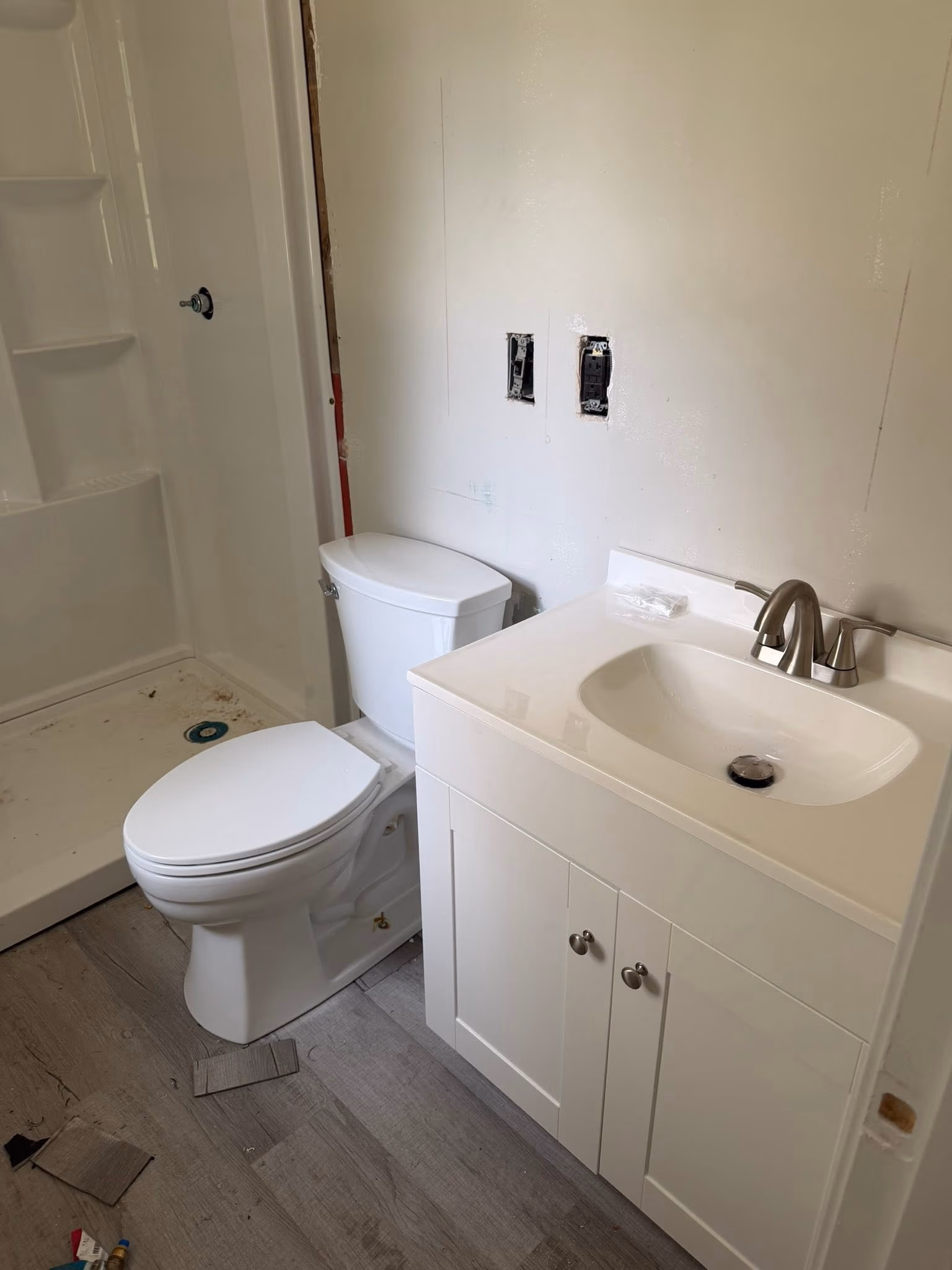 Small bathroom with white toilet, white vanity with sink, and an unfinished shower stall.