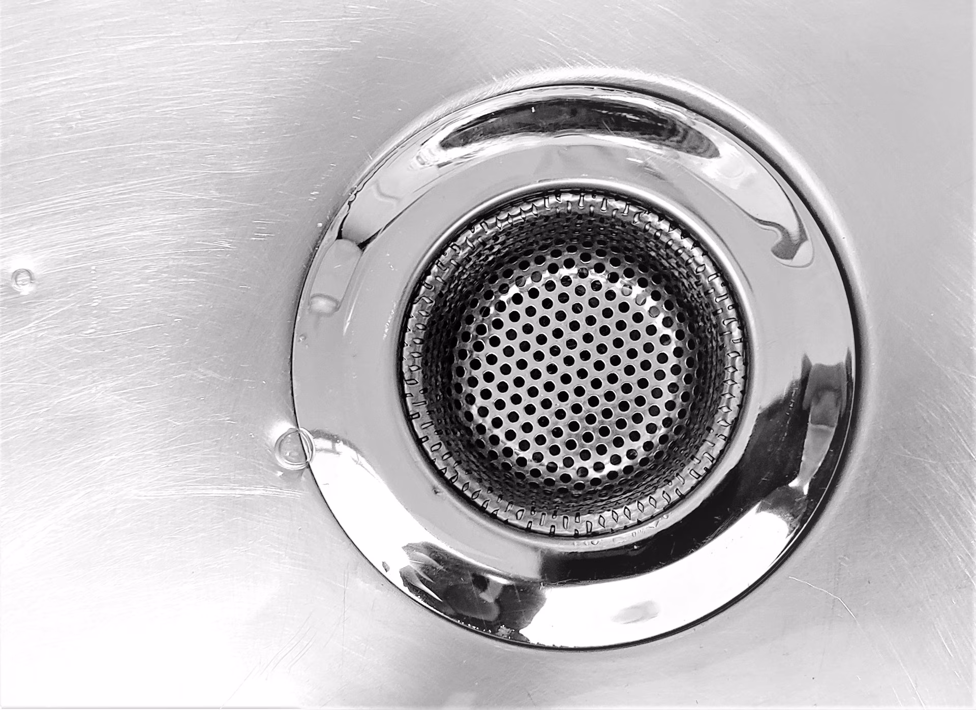 Close-up of a clean stainless steel sink drain with a perforated strainer in the center.