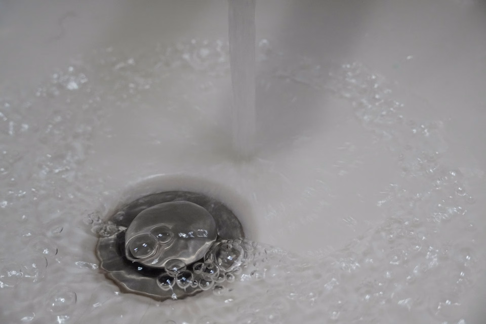 Water flowing down a sink drain with bubbles around the drain stopper.