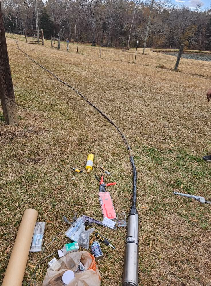 Long black cable connected to a metal pump on grass with tools and supplies scattered nearby.
