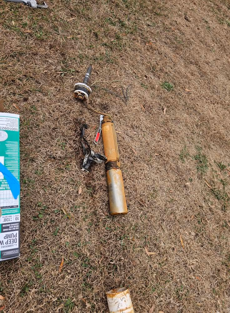 Rusty submersible pump lying on dry grass next to a green box with labels.