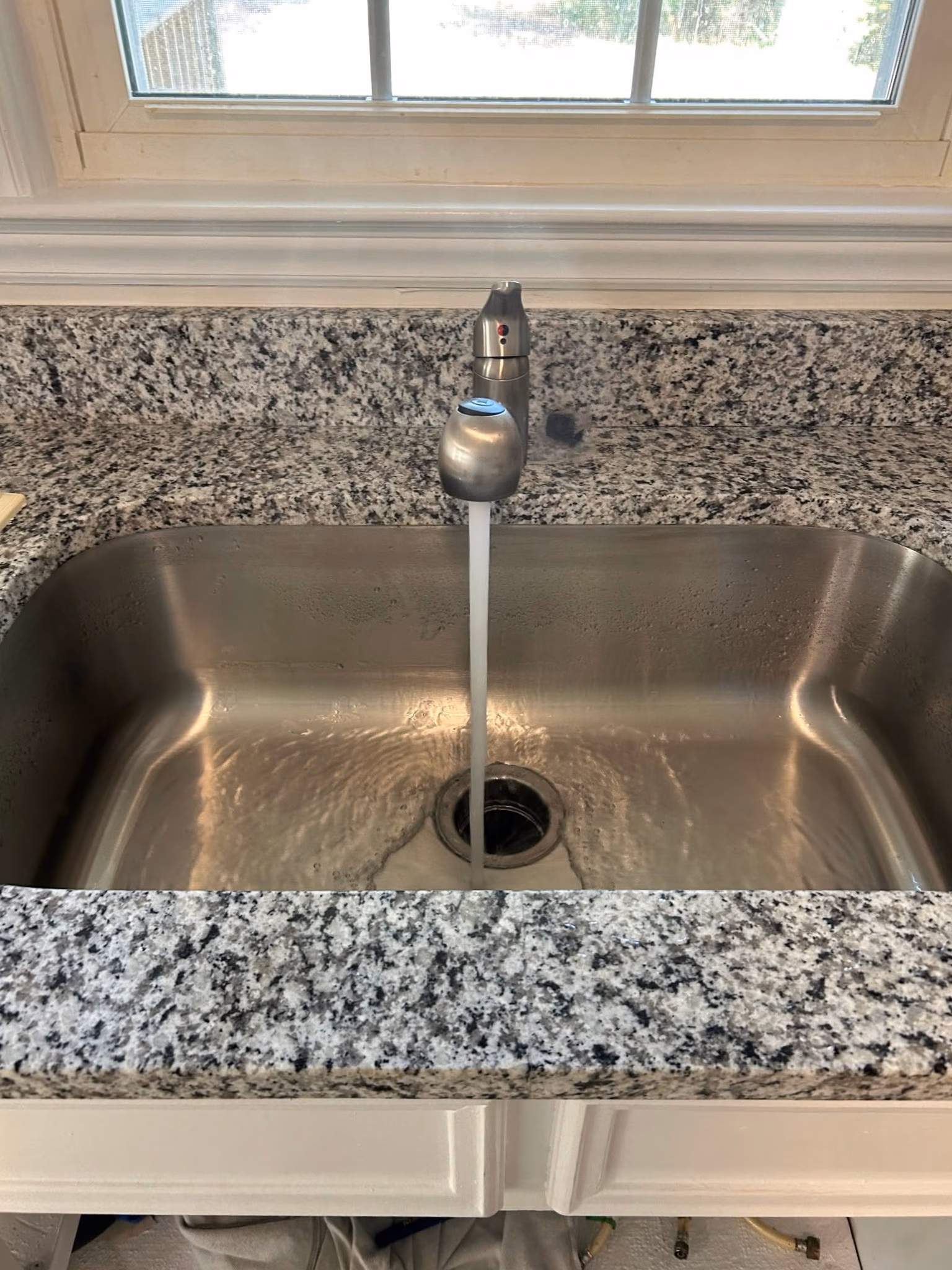 Stainless steel kitchen sink with running water from a single-handle faucet under a window.