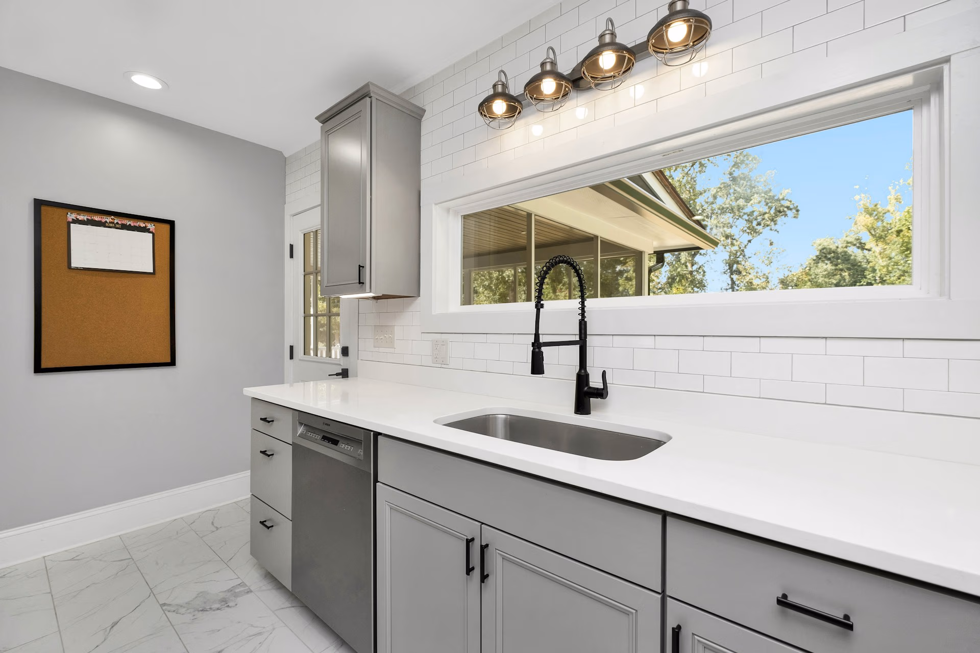 Modern kitchen sink with matte black faucet, gray cabinets, white countertop, and large window.