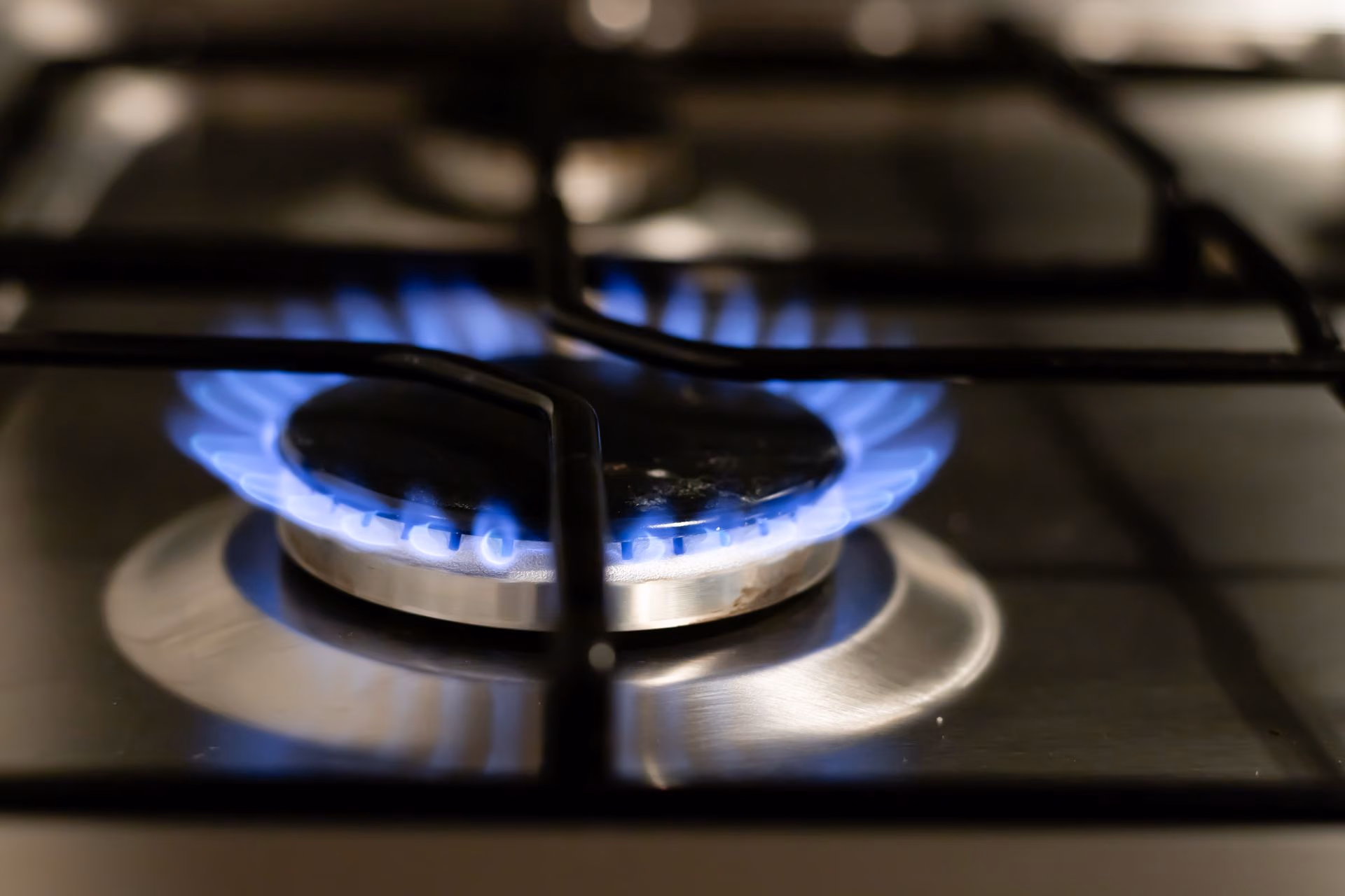 Close-up of a blue flame burning on a stainless steel gas stove burner with black grates.