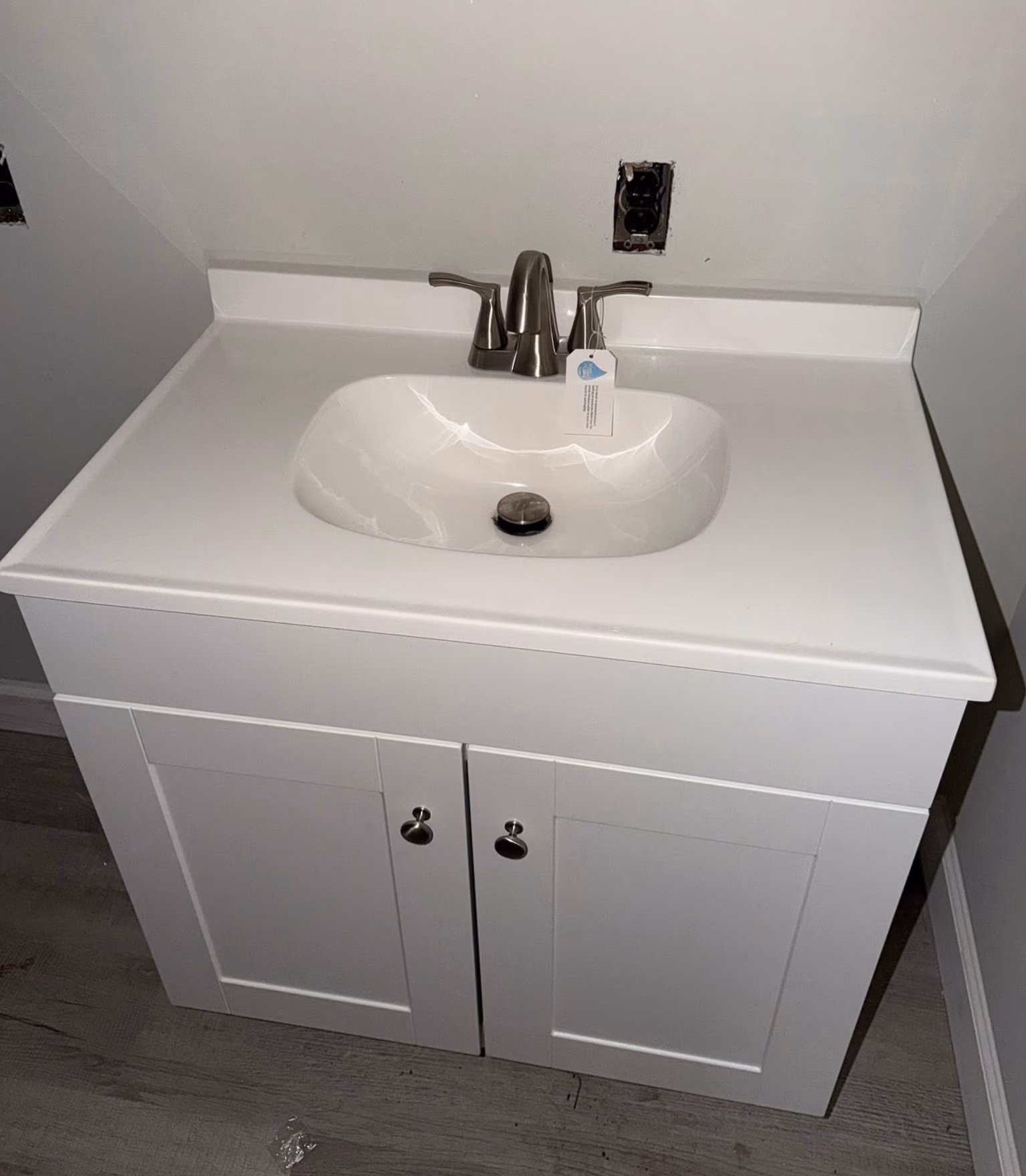White bathroom vanity with built-in sink, silver faucet, and two cabinet doors on a wood floor.
