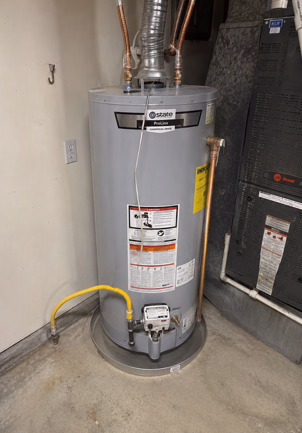 Gray State ProLine commercial-grade water heater with pipes and warning labels in a utility room.
